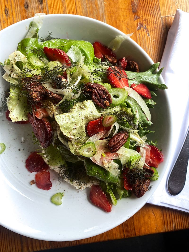 Butterhead salad with strawberries and cheese on a white dish at Foreign and Domestic restaurant.